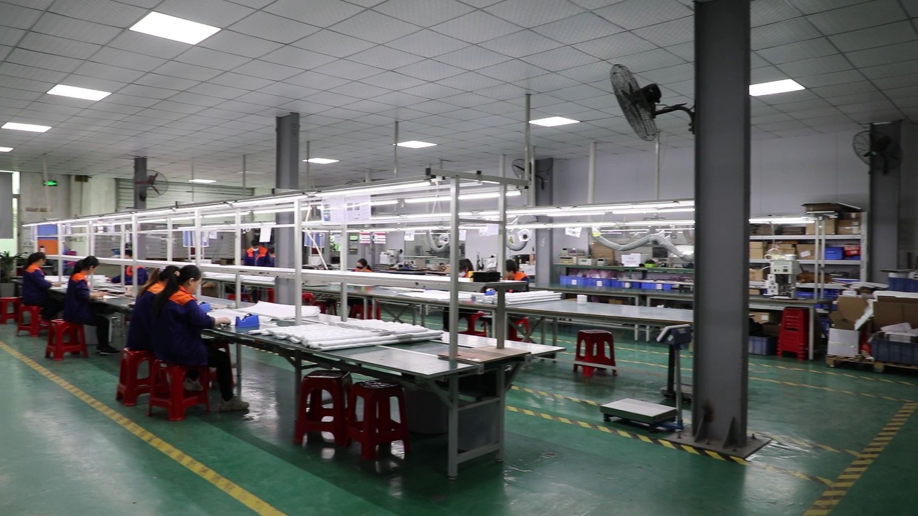 Workers seated along a long production bench in a bright factory hall