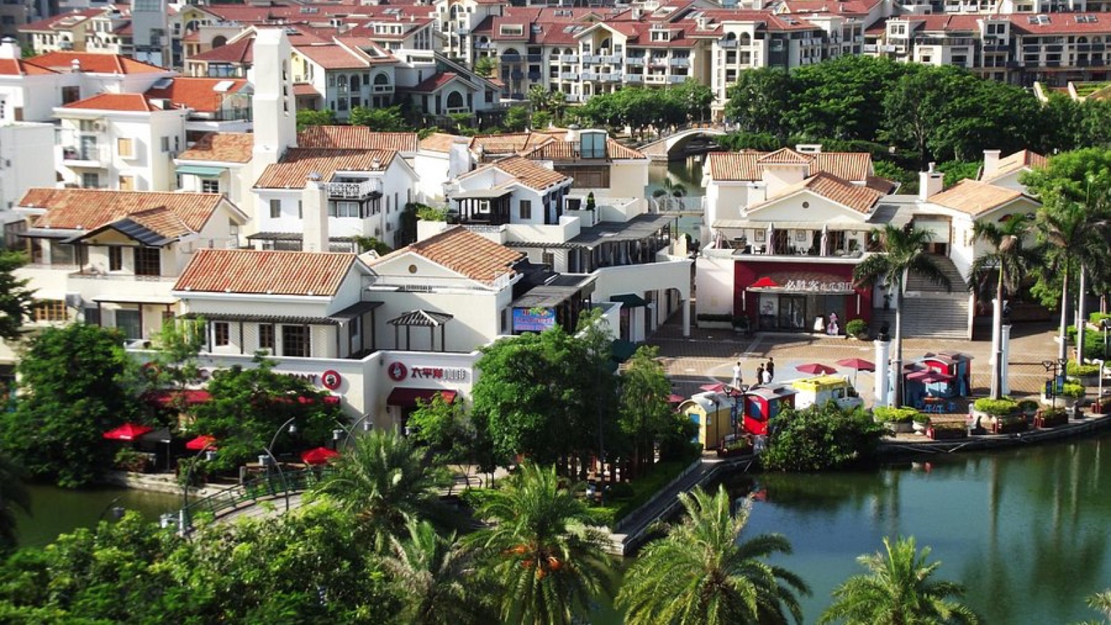 White villas with red tile roofs, shops and cafes along a canal, with palm trees