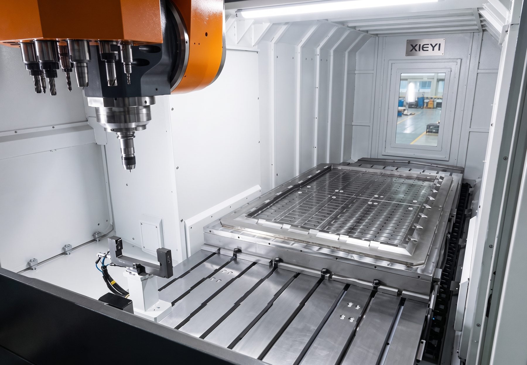 Inside a 5-axis machining center with an orange spindle head, tool holders and a large machine table